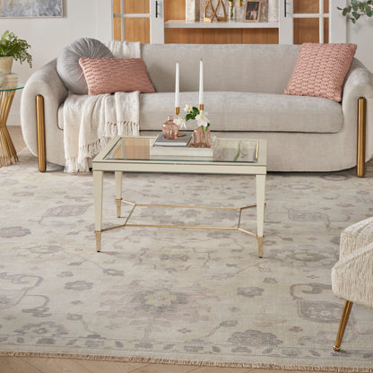 Beige fabric sofa with pink cushions and cream throw, glass coffee table with gold frame, soft patterned rug.