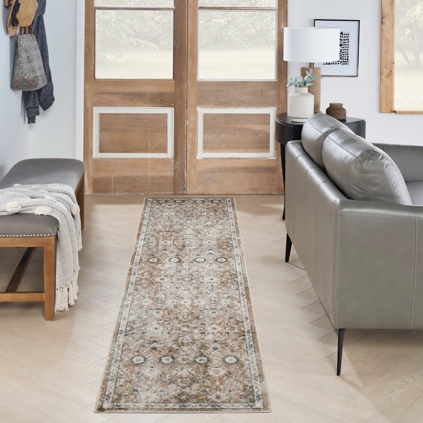 Long beige patterned rug runner with blue accents in a modern entryway beside a gray leather sofa.