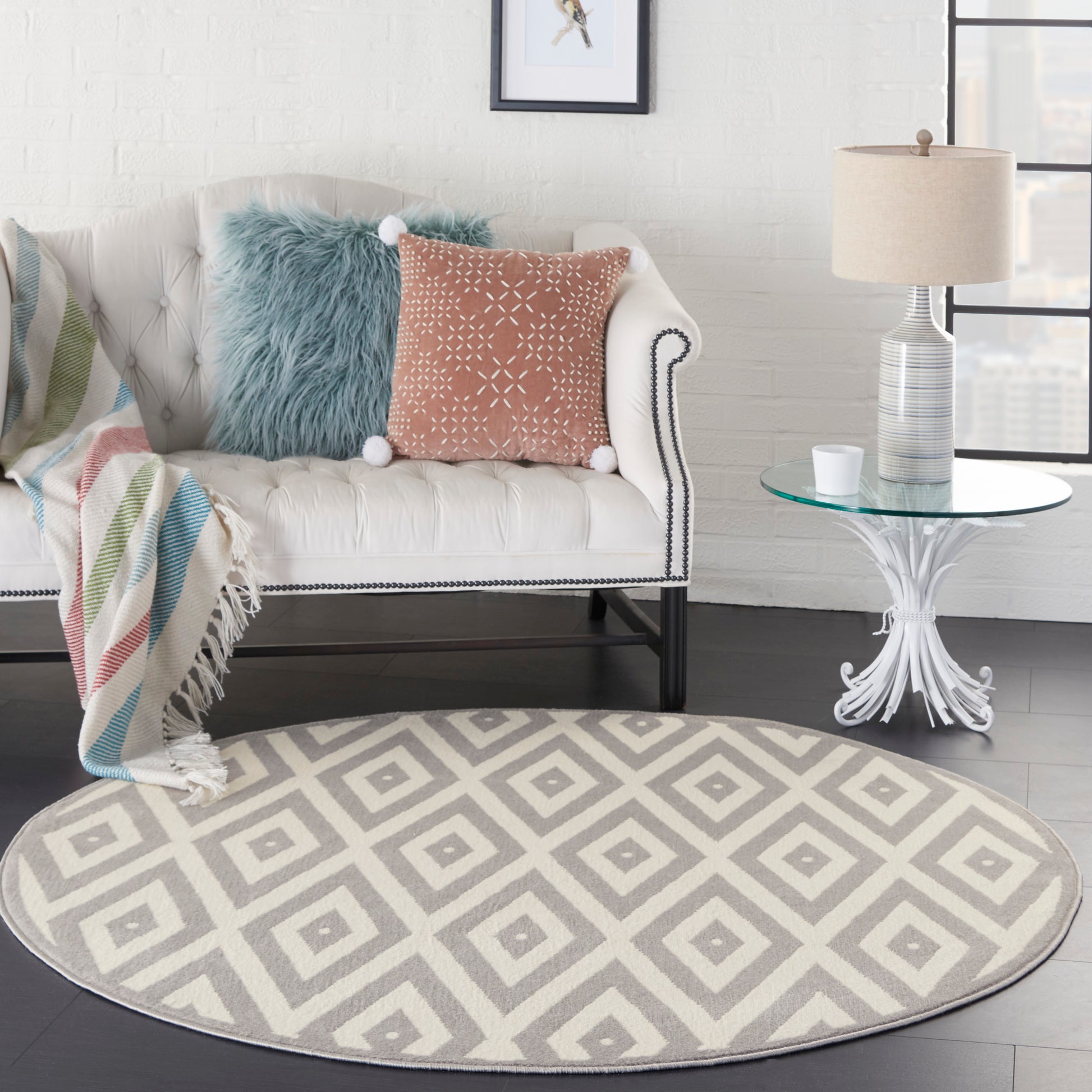 Round gray-and-ivory geometric rug under a white tufted sofa with blue faux-fur pillow, rust cushion and striped throw.