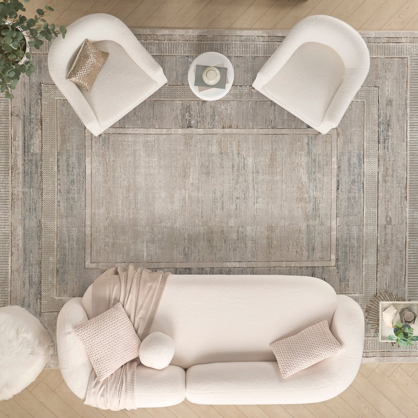 Top-down view of a living room with a gray rug under a curved beige sofa, two white armchairs, and a coffee table.