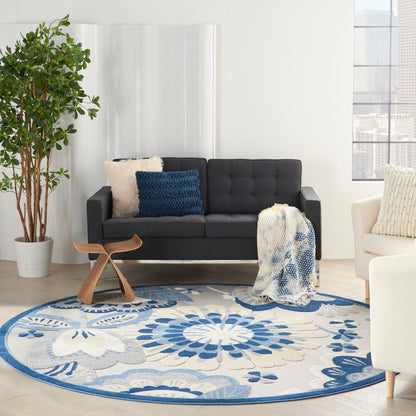 Round blue floral rug in a bright living room with a dark gray sofa, throw blanket, blue pillows, and wood accent table.