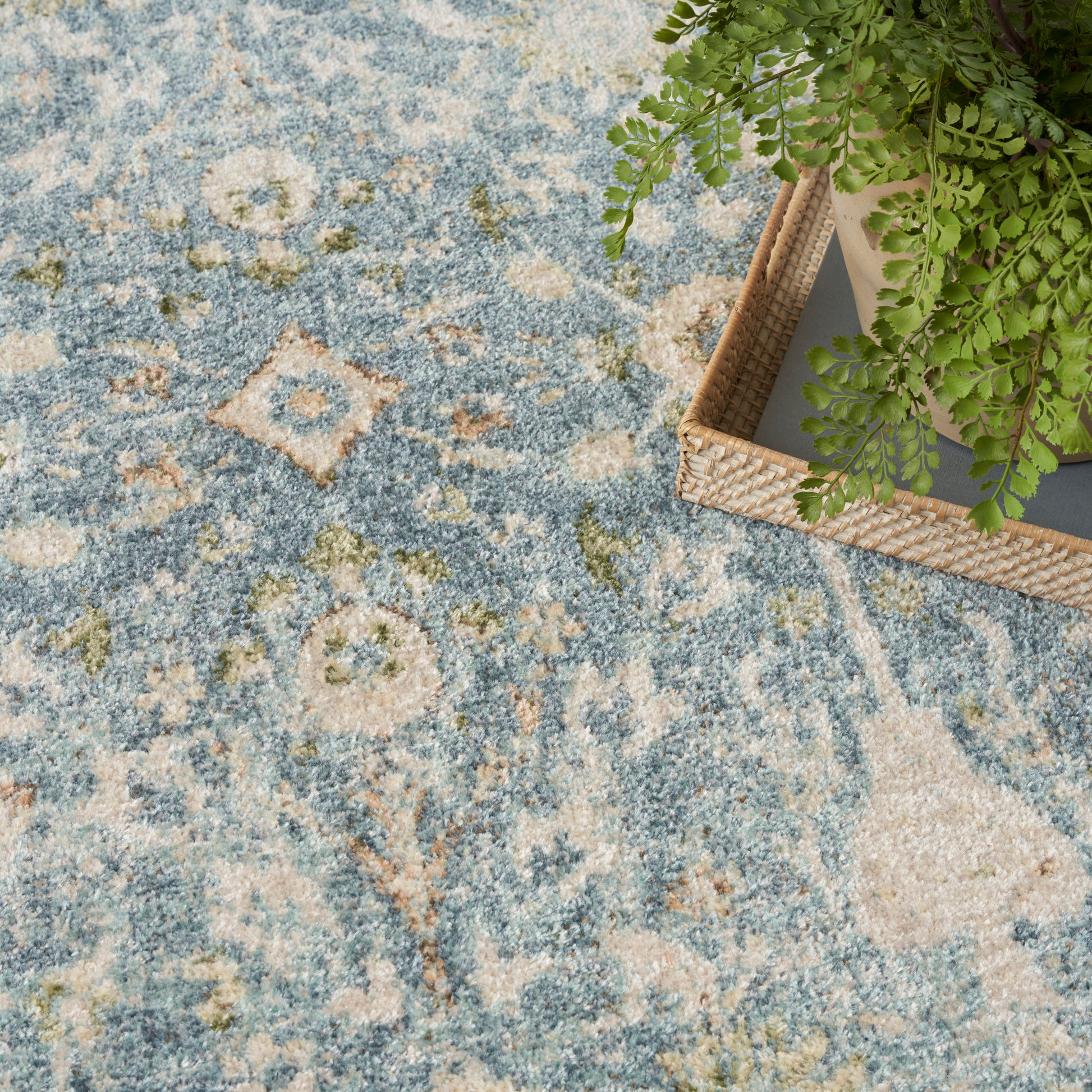 Blue distressed oriental rug with cream geometric motifs; natural wicker basket with green plant on the edge.