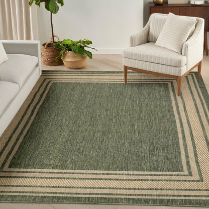 Green rectangular area rug with beige striped border in a cozy living room beside a cream striped armchair and potted plants.