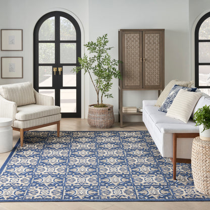 Coastal living room with blue and ivory patterned area rug, cream armchair, white sofa, arched black doors, woven cabinet.