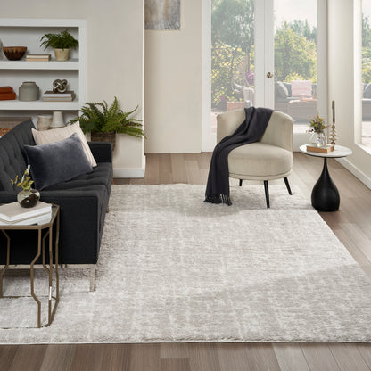 Modern living room with light gray rug, charcoal sofa, round beige chair, dark throw, and gold-framed side table.