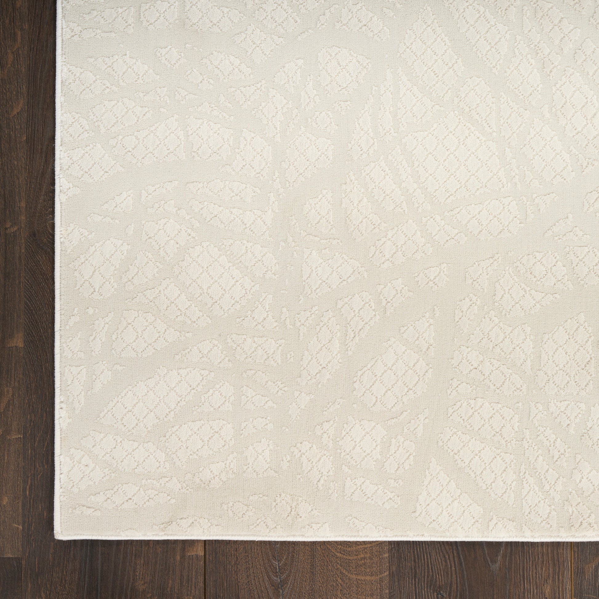 Rectangular beige area rug with a subtle raised botanical pattern on dark wood flooring.