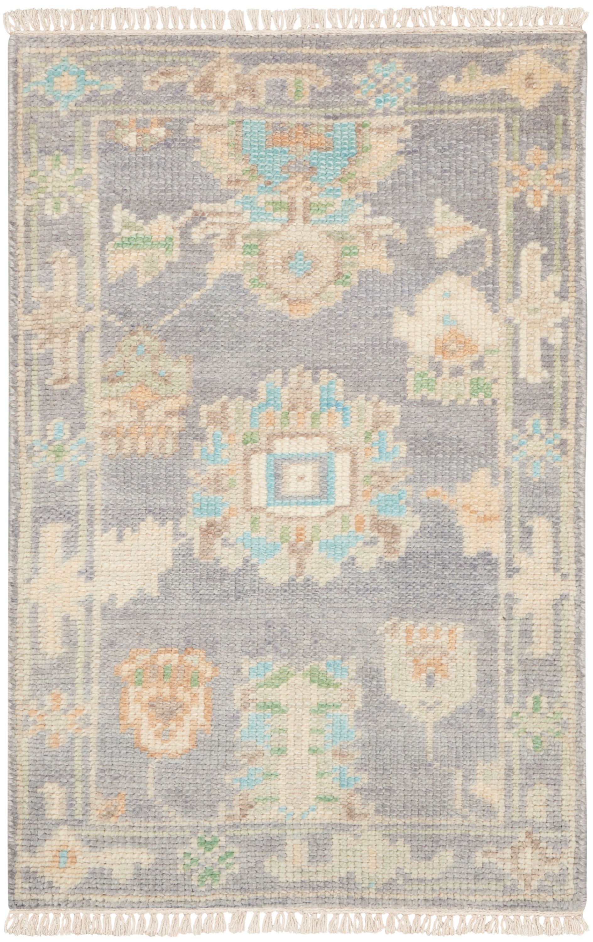 Lavender-gray woven rug with pastel cream, peach and turquoise floral medallions and fringed edges.