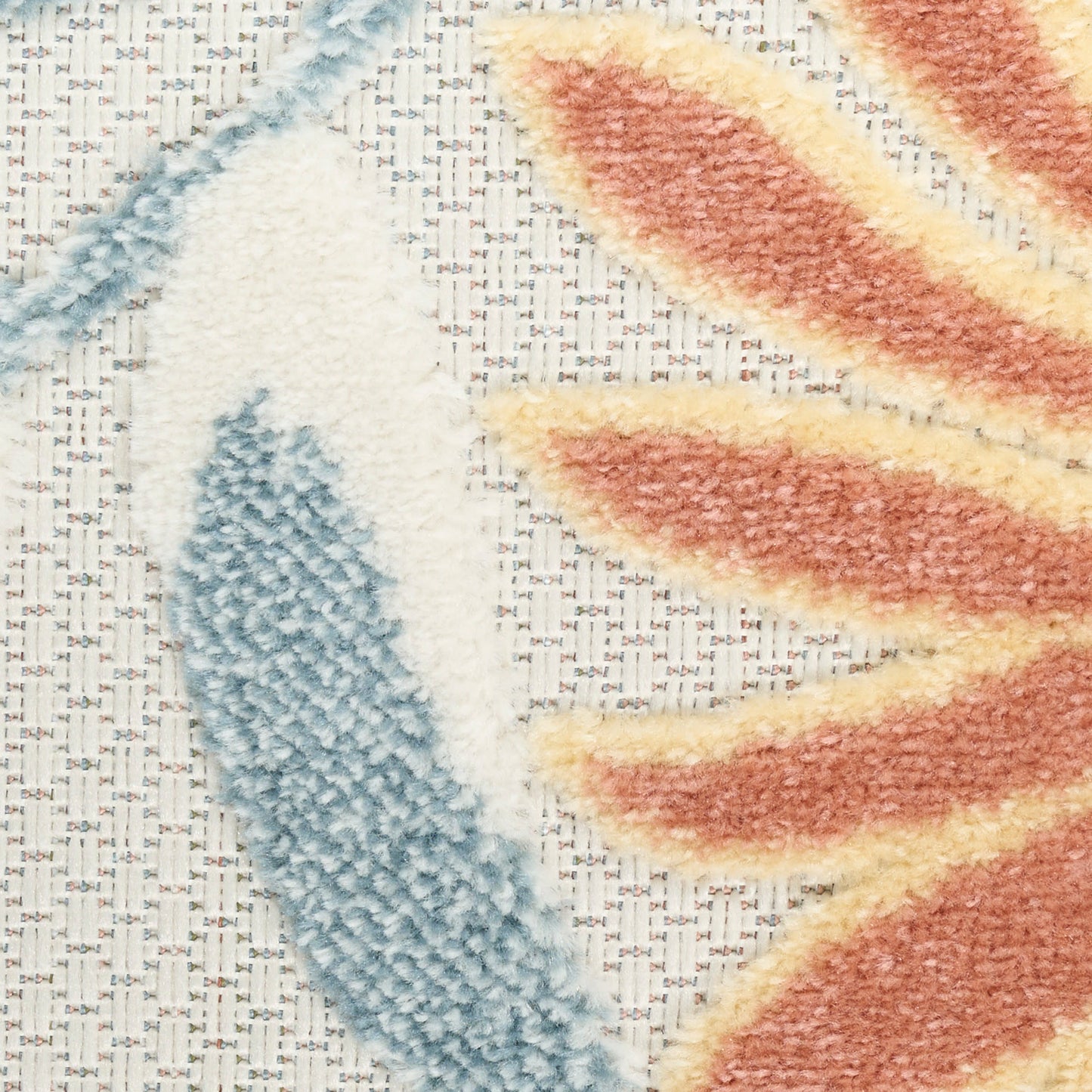 Close-up of a tufted rug featuring a blue leaf motif and orange-yellow leaf motif on a woven beige backing.