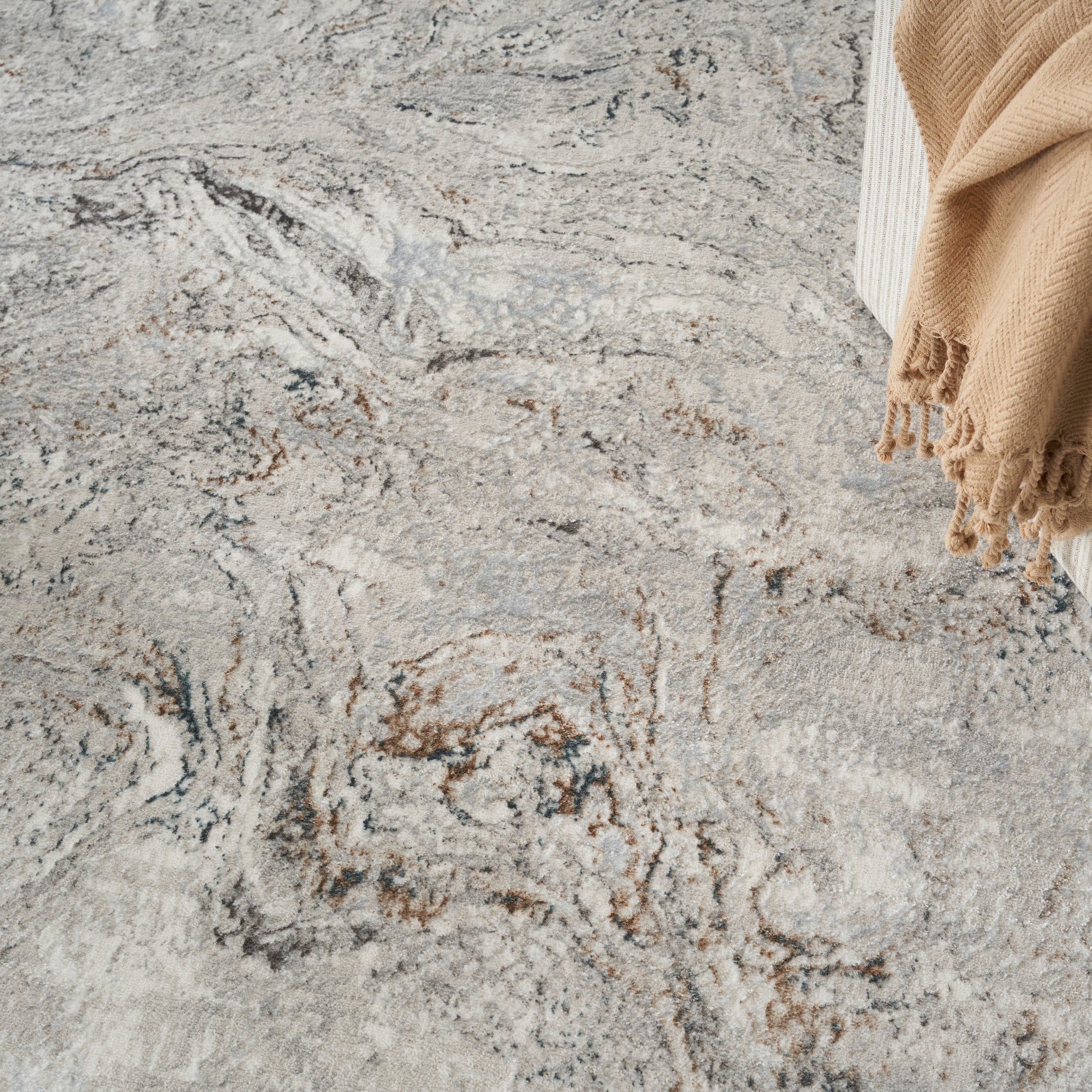 Abstract gray-beige area rug with brown veining; beige fringed throw at corner.