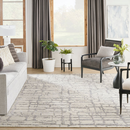 Bright modern living room with grey sofa, rug, black-framed chairs, potted plants, & large window with dark curtains.
