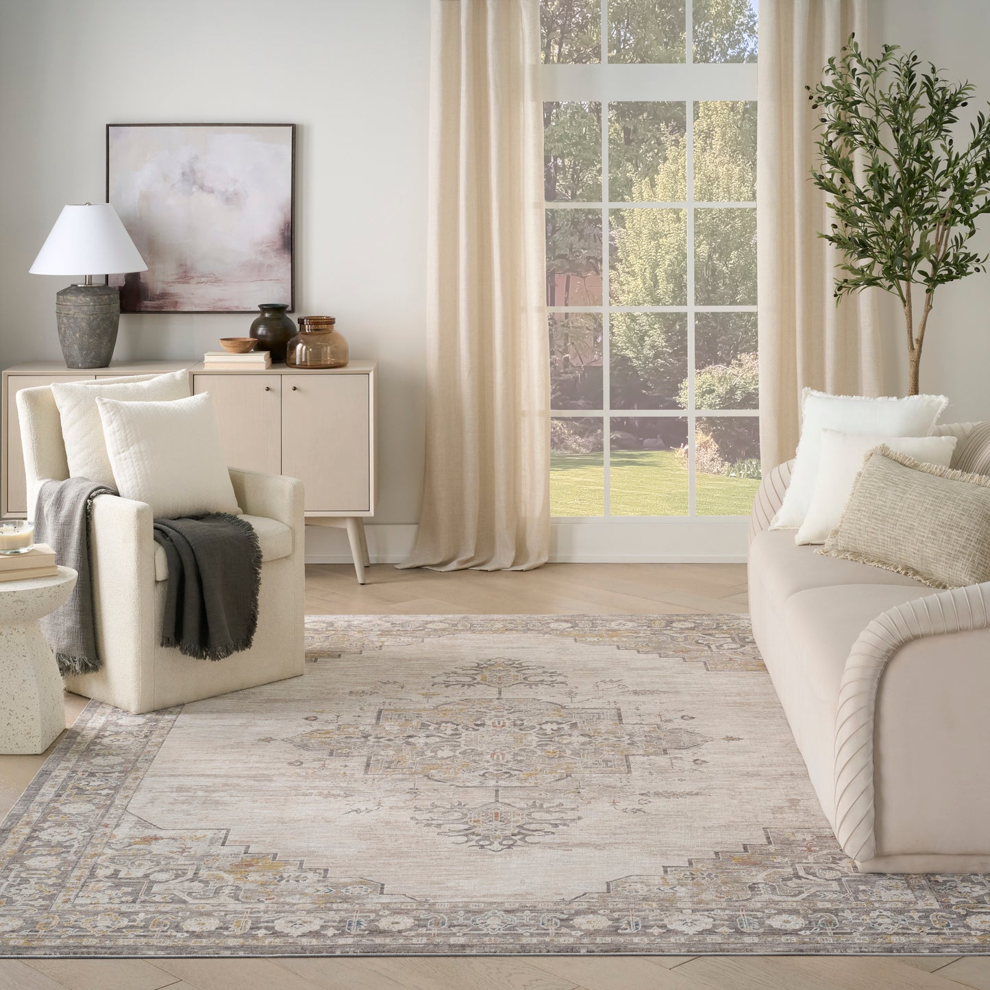 Neutral living room with cream sofas, beige armchair, rug, cabinet, lamp, and large window with sheer curtains.