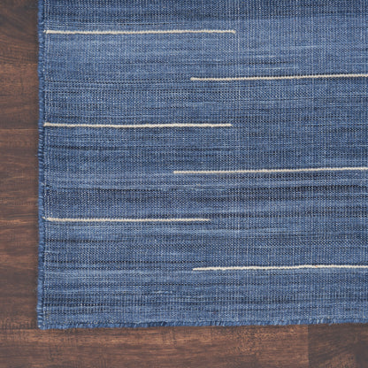 Rectangular blue denim-look woven rug with thin beige horizontal stitches on a wooden floor.