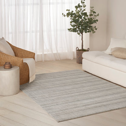 Bright living room with light gray striped rug, white sofa, wicker chair, potted plant, and sheer curtains.