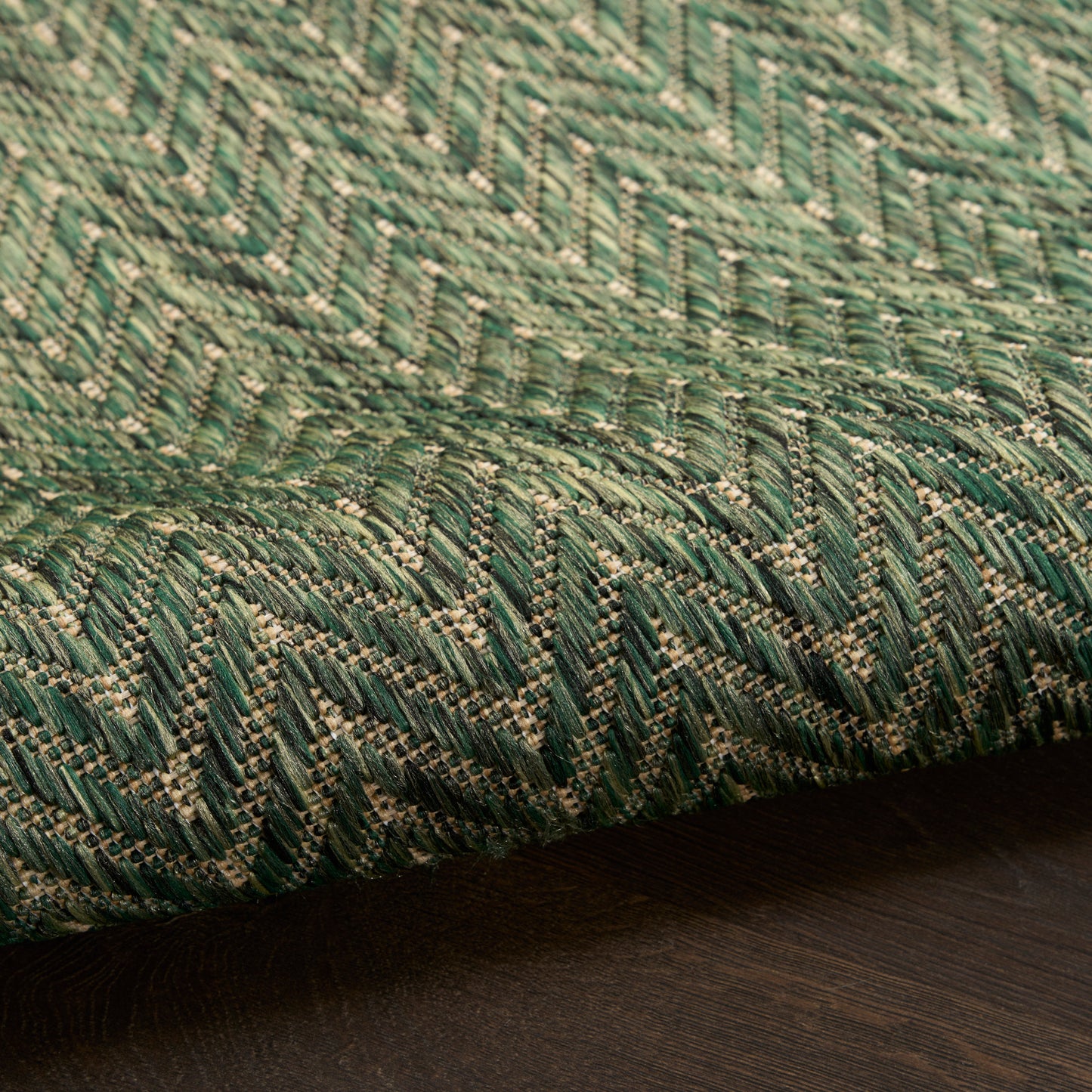Green woven rug with a chevron zigzag pattern in dark and light greens, folded on a dark wooden surface.