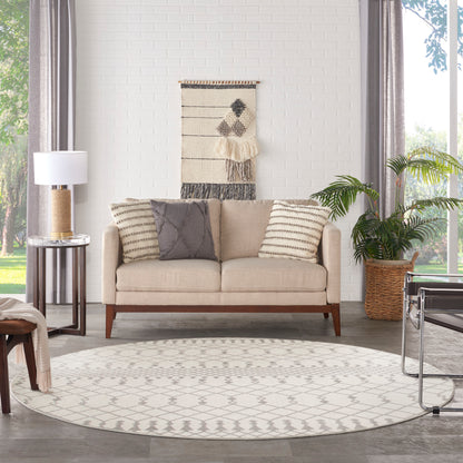 Beige mid-century sofa with striped and grey cushions on a round geometric rug; woven wall hanging, lamp, and potted plant.