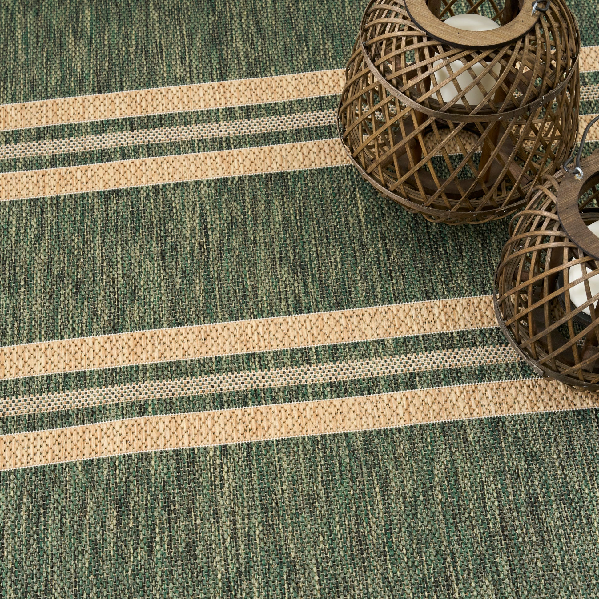 Green and beige striped woven rug with two brown wicker lanterns resting on it.