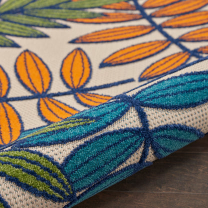 Close-up of a woven rug with orange leaf motifs and teal-blue leaves on beige, folded edge.