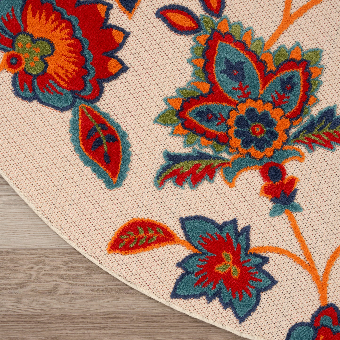 Cream round rug with bold orange, red, teal and blue floral motif and woven texture.