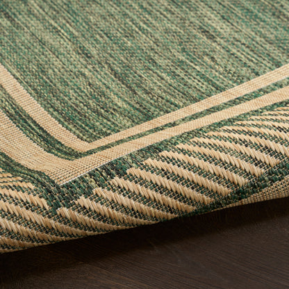 Green woven rug with beige border, folded corner on dark wood floor.