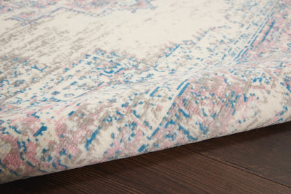Close-up of a plush beige rug with pink and blue distressed pattern, rolled at the edge on a dark wood floor.