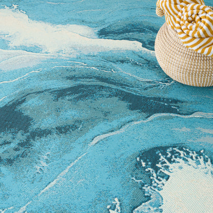 Turquoise wave-pattern beach towel with a woven straw hat and a yellow-white striped towel draped on the edge