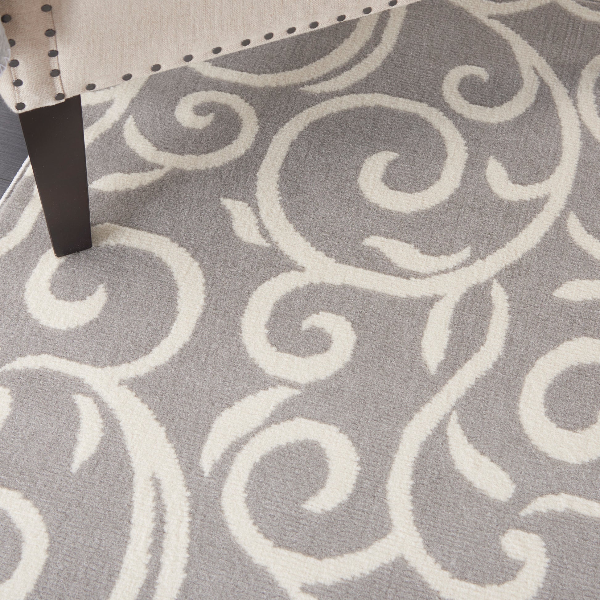 Gray rug with ivory-white scrollwork pattern, under a dark furniture leg.