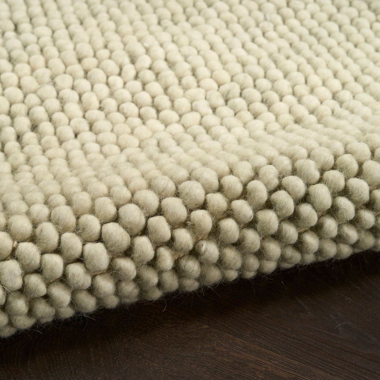 Cream boucle rug with dense bubble tuft texture on dark wooden floor.