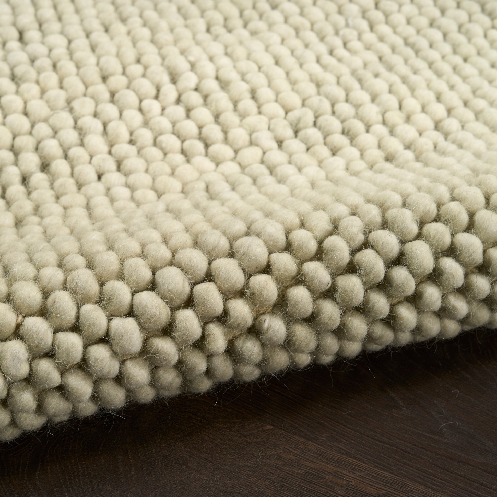 Cream boucle rug with dense bubble tuft texture on dark wooden floor.