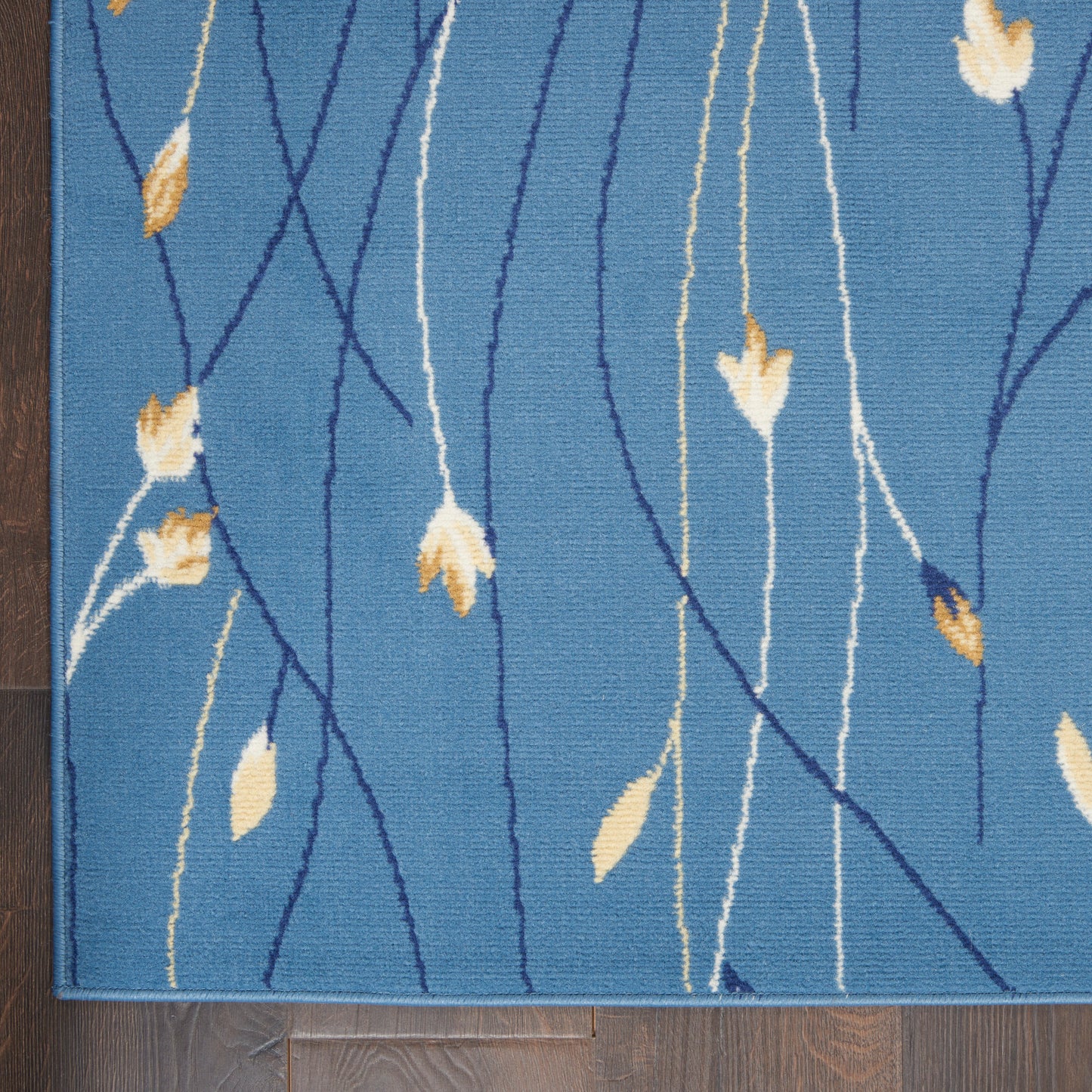 Blue rectangular rug with cream and navy abstract vertical lines and pale yellow leaf motifs on a wooden floor.