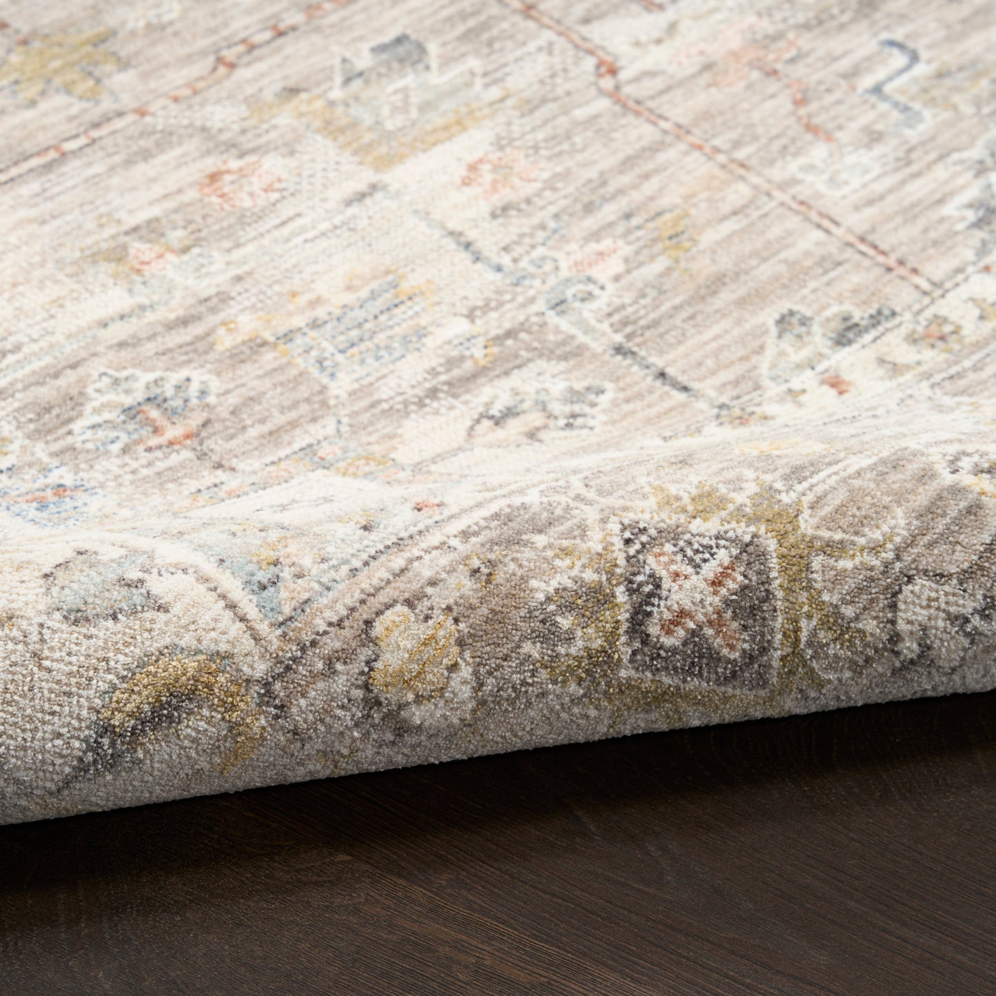 Soft neutral woven rug with a muted medallion pattern, folded corner reveals plush pile and pastel accents.
