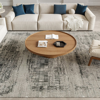 Gray 8' x 10' modern rug in a living room setting with a beige sofa and blue cushions; round wood coffee table with books, magazines, and a black hex tray.