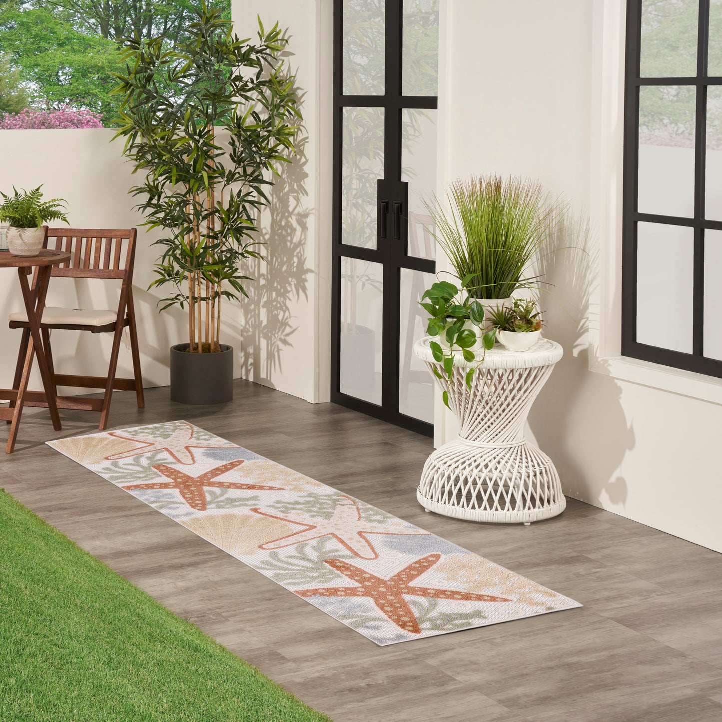 Long indoor-outdoor runner rug with orange starfish motif on beige background, beside glass doors with potted plants.