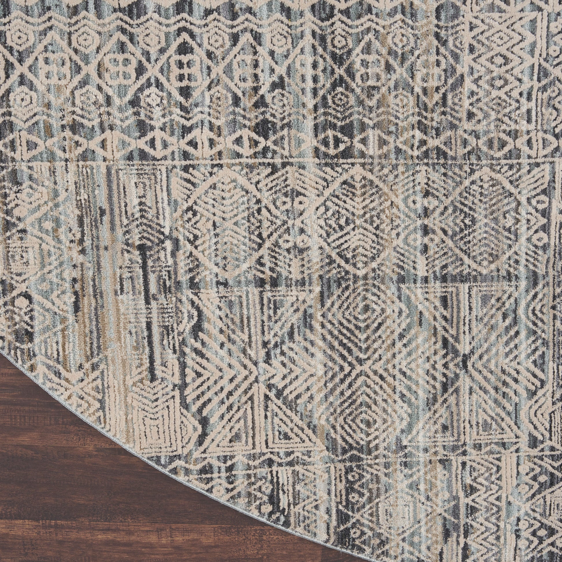 Muted blue and beige geometric patterned area rug with tribal motifs on wood floor; curved corner visible.
