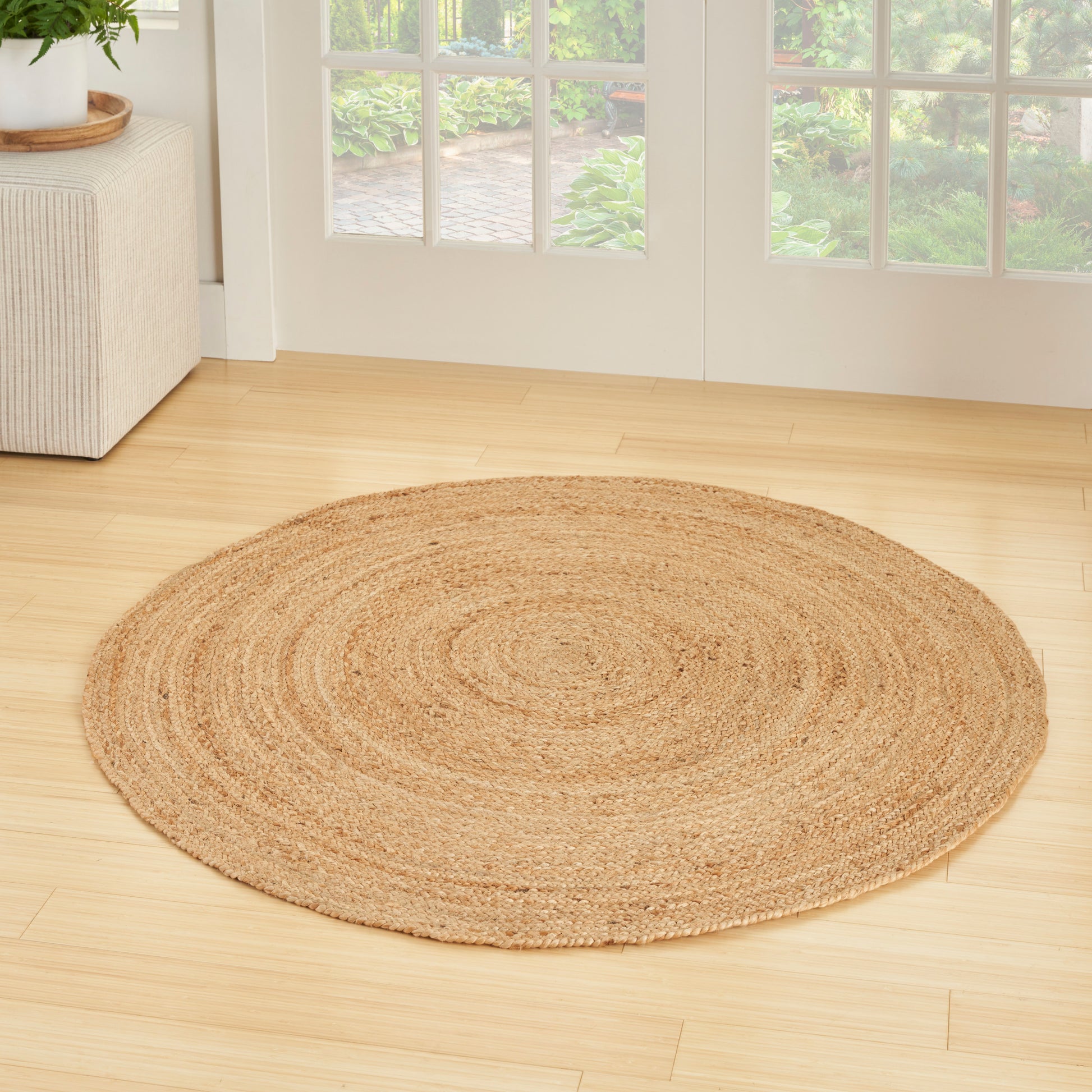 3' round natural jute braided rug in beige tones on a light wood floor in a bright living room.