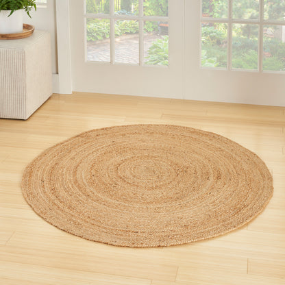 3' round natural jute braided rug in beige tones on a light wood floor in a bright living room.