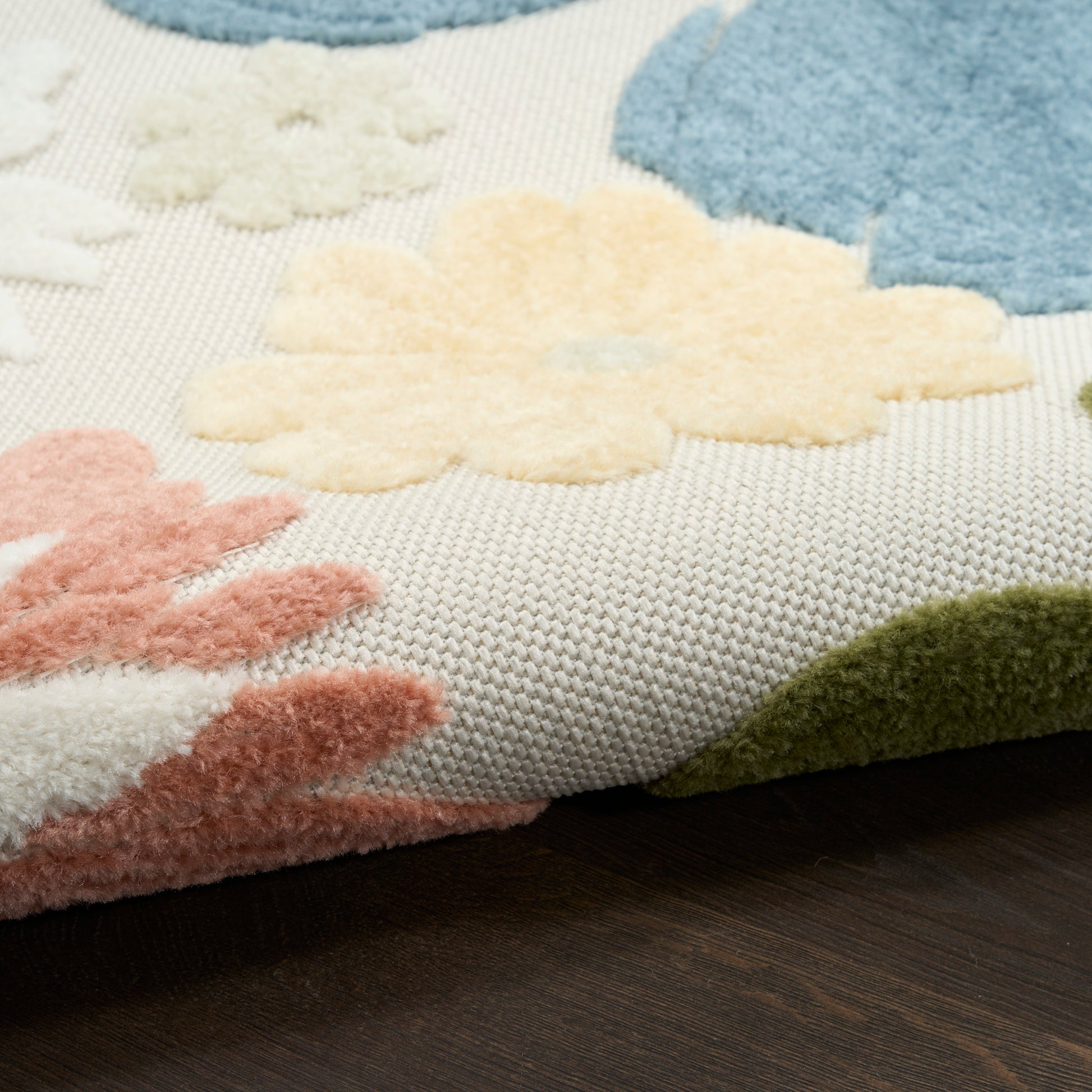 Fluffy tufted floral rug with pastel petals in cream, pink, blue and green on a light woven base on a dark wood floor.