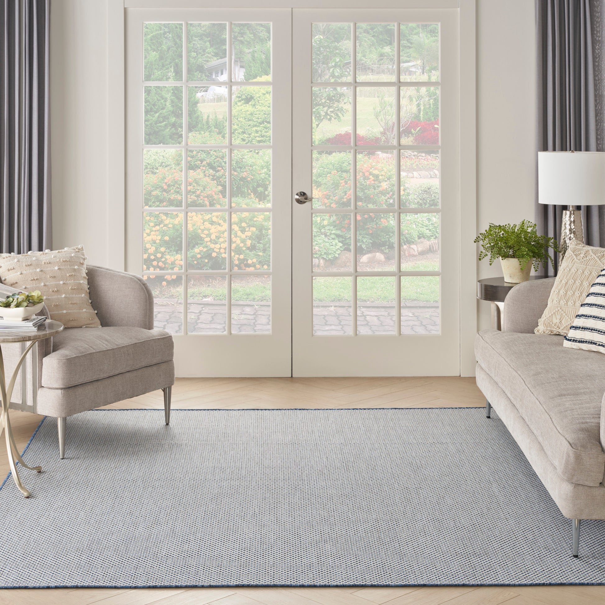 Cream-beige fabric armchair and sofa, gray-blue textured rug, white French doors with glass panes, bright cozy living room.
