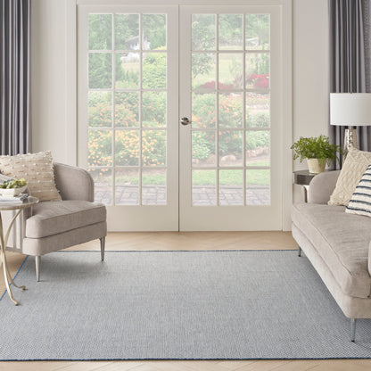 Cream-beige fabric armchair and sofa, gray-blue textured rug, white French doors with glass panes, bright cozy living room.