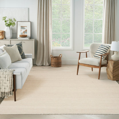 Bright, airy living room with beige rug, light gray sofa, mid-century wooden chair, striped pillow, woven basket, framed art.