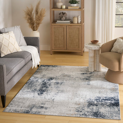Abstract blue-gray area rug in a modern living room with grey sofa, beige chair, light wood floor, woven cabinet.