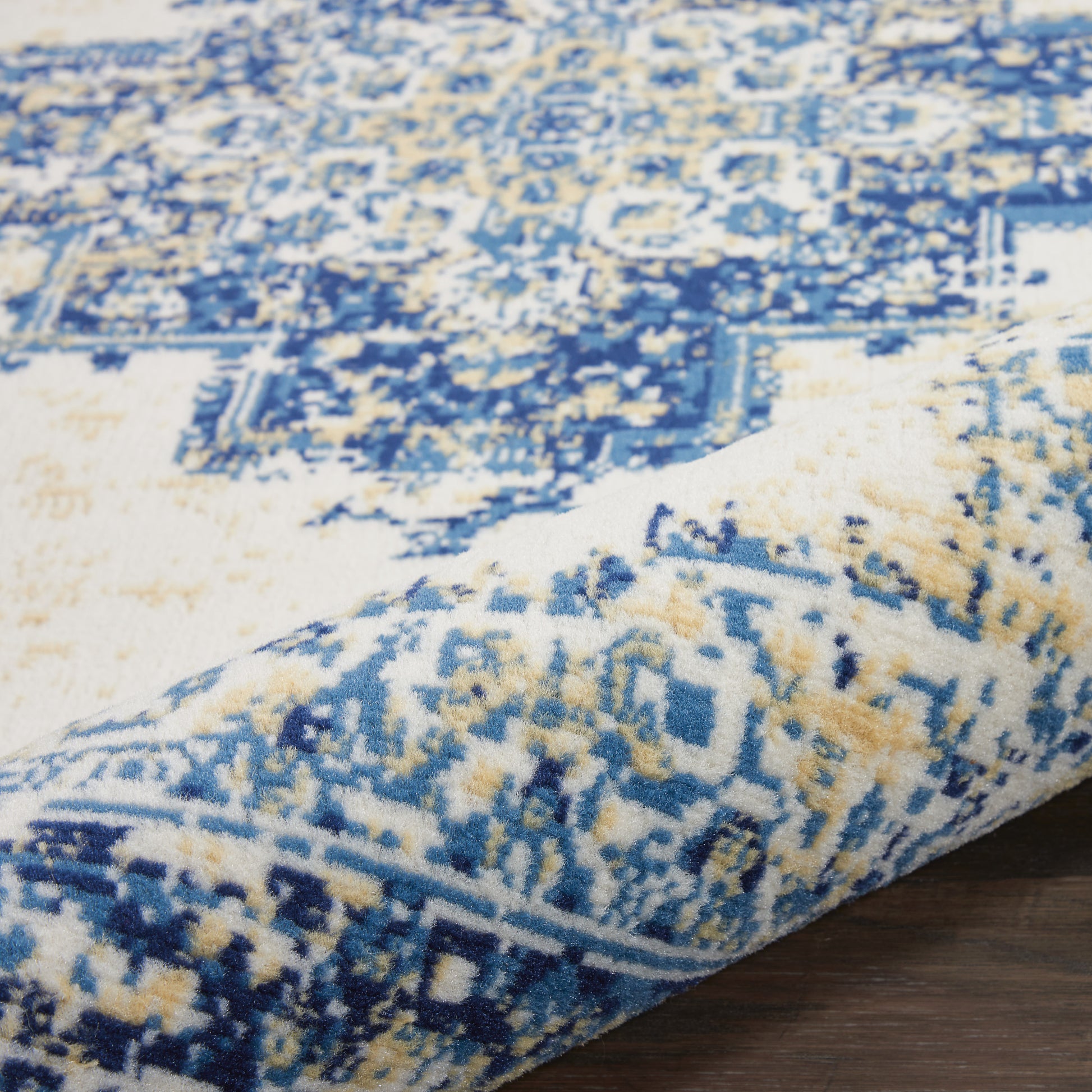 Close-up of a blue and ivory geometric patterned rug with a rolled edge on a wooden floor.