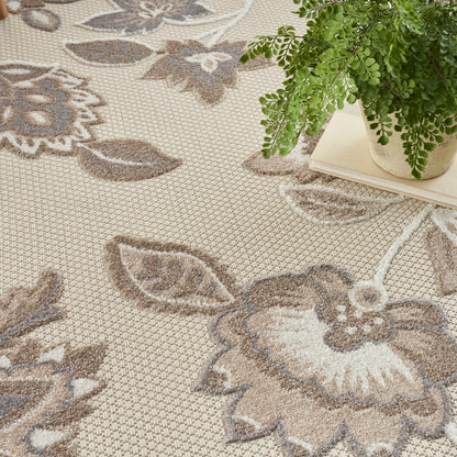 Beige floral patterned area rug with brown leaf & flower motifs; soft woven texture, potted plant on books nearby.