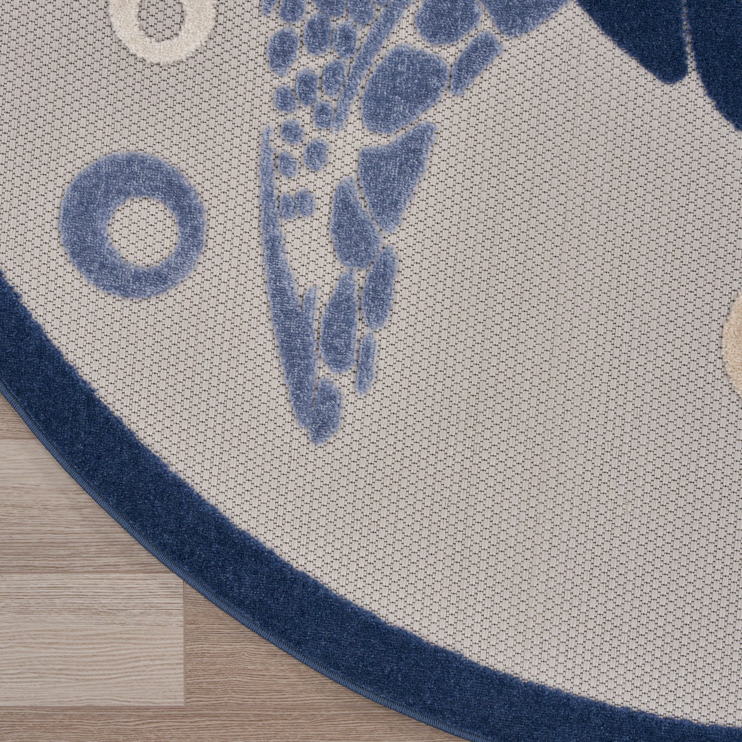 Round beige rug with navy border, blue leaf motif and circular shapes; woven texture on wood floor.
