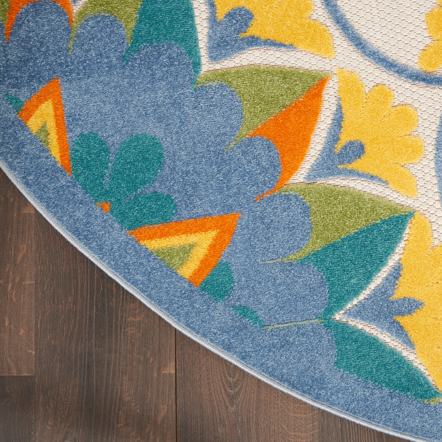 Round multicolor rug with blue, teal, yellow and orange floral motif, soft tufted pile on dark wood floor.