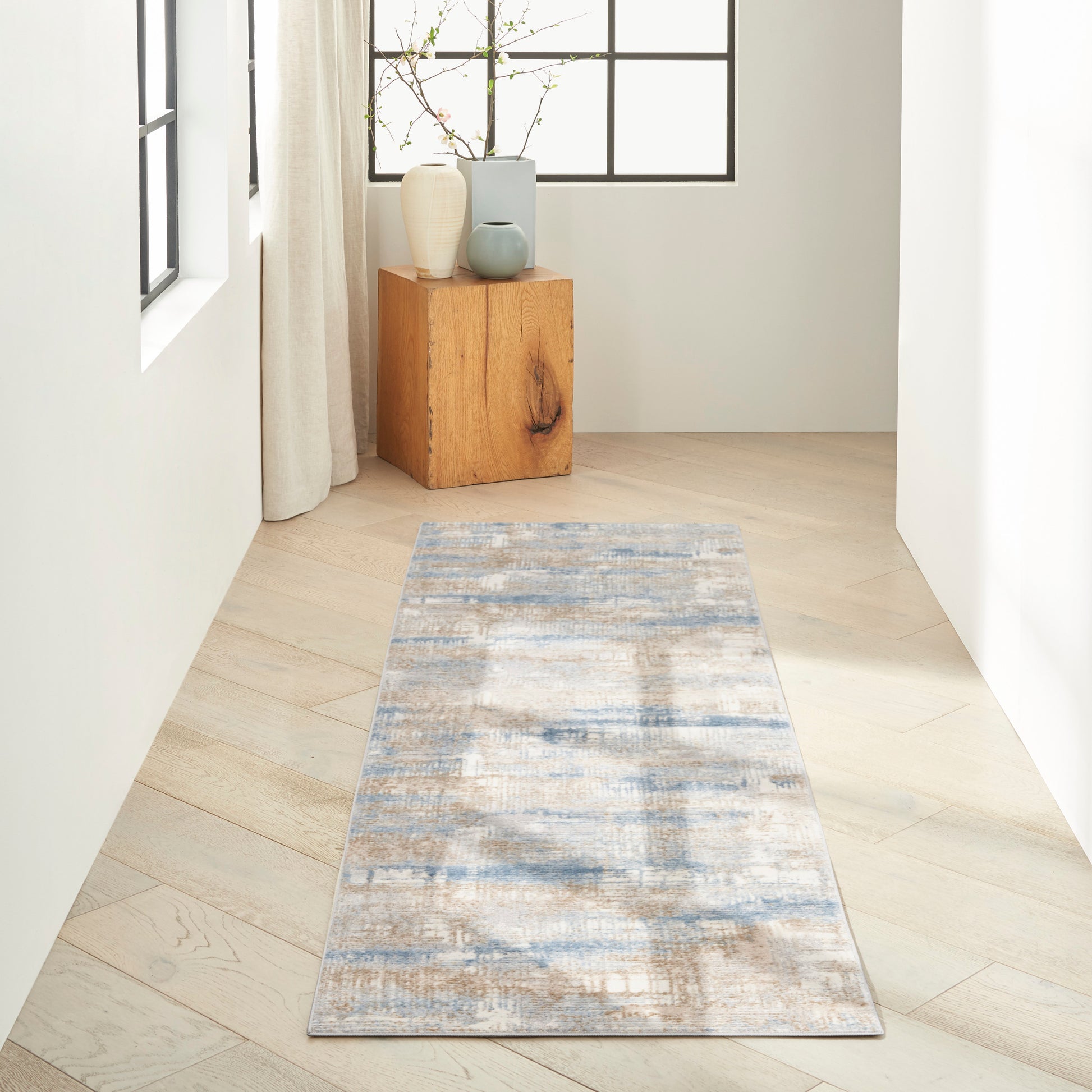 Blue-gray patterned runner rug on light wood flooring with a wooden block table and ceramic vases by a window.