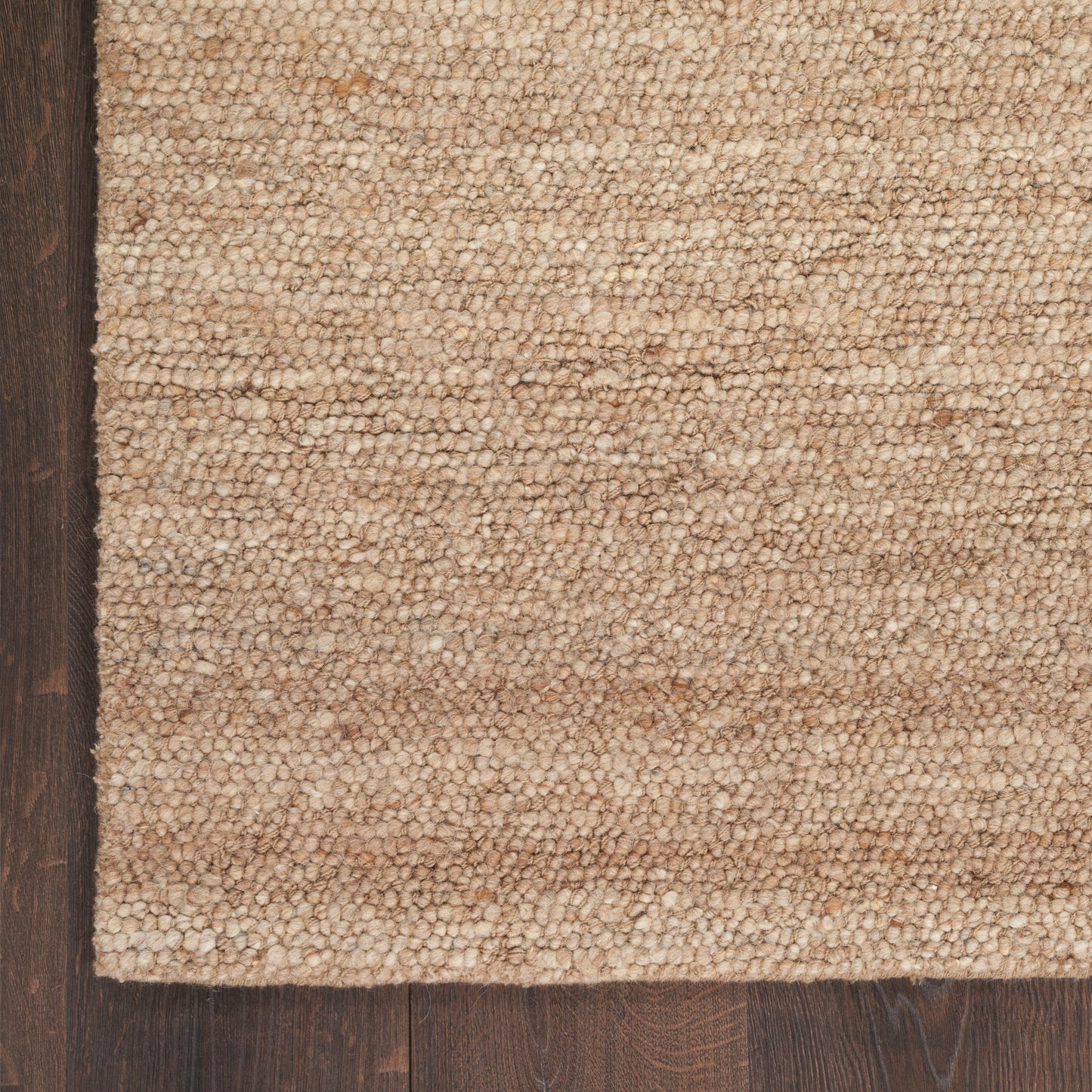 Beige textured loop-pile rug edge on dark wood floor; cozy neutral-toned home decor.