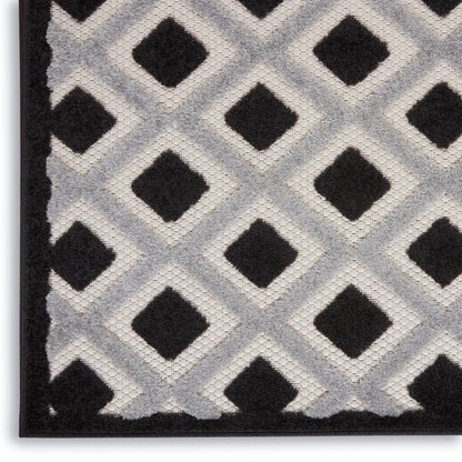 Close-up of a geometric rug featuring black diamond motifs on a light gray lattice with a black border.