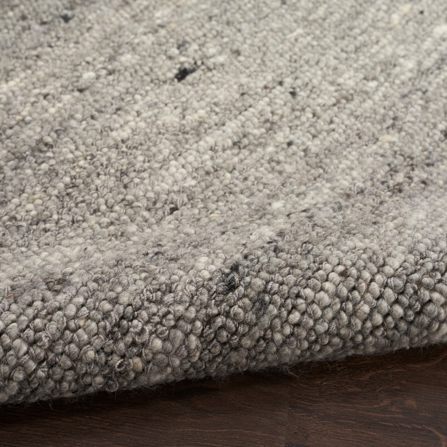 Gray speckled loop-pile rug with soft, chunky fibers on dark wood floor.