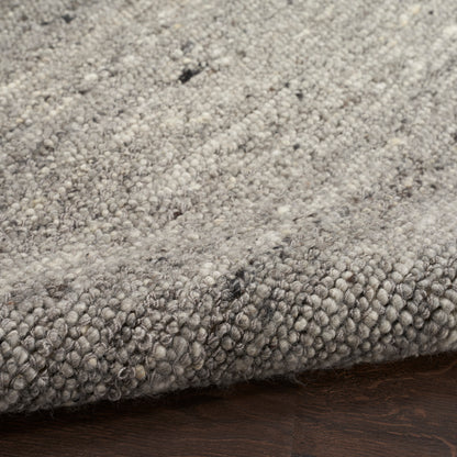 Gray speckled loop-pile rug with soft, chunky fibers on dark wood floor.