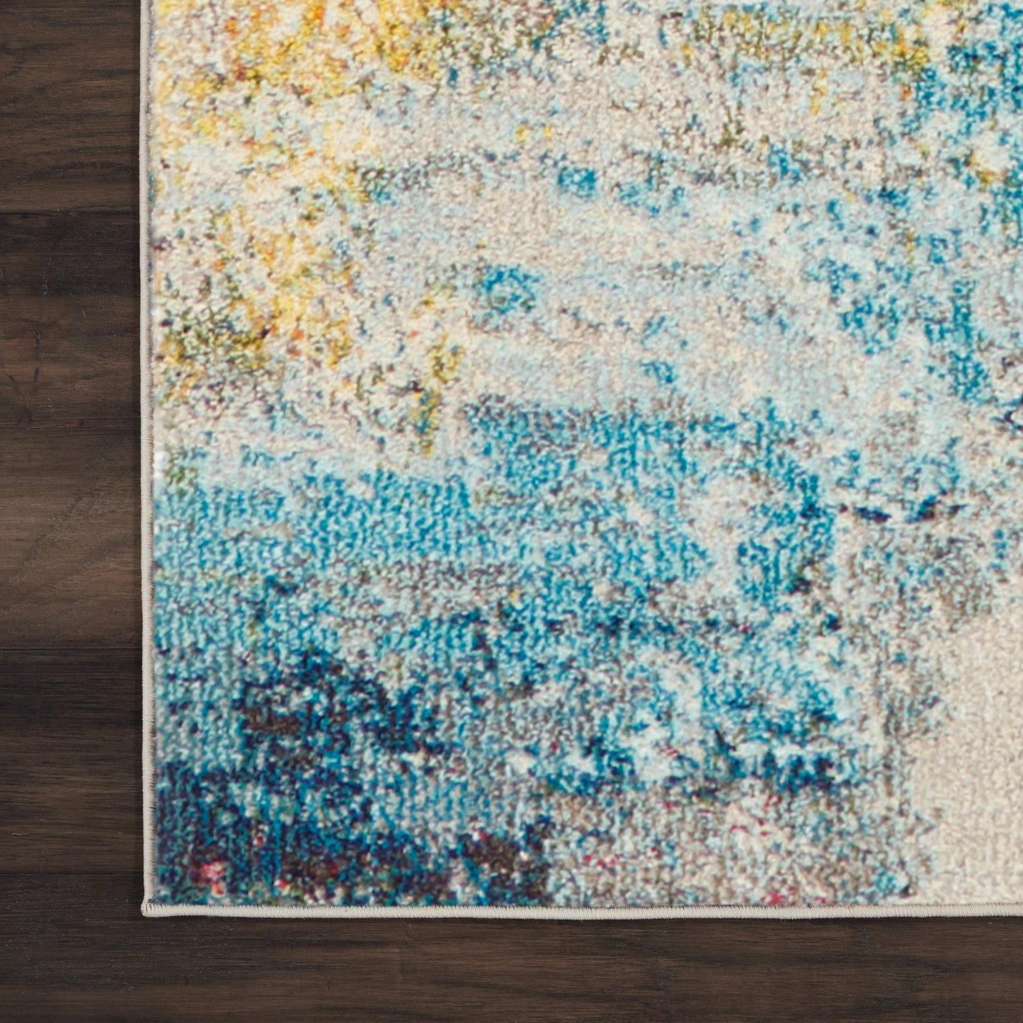 Abstract multicolor area rug featuring yellow, teal, and blue hues on a cream base, on dark wood floor.